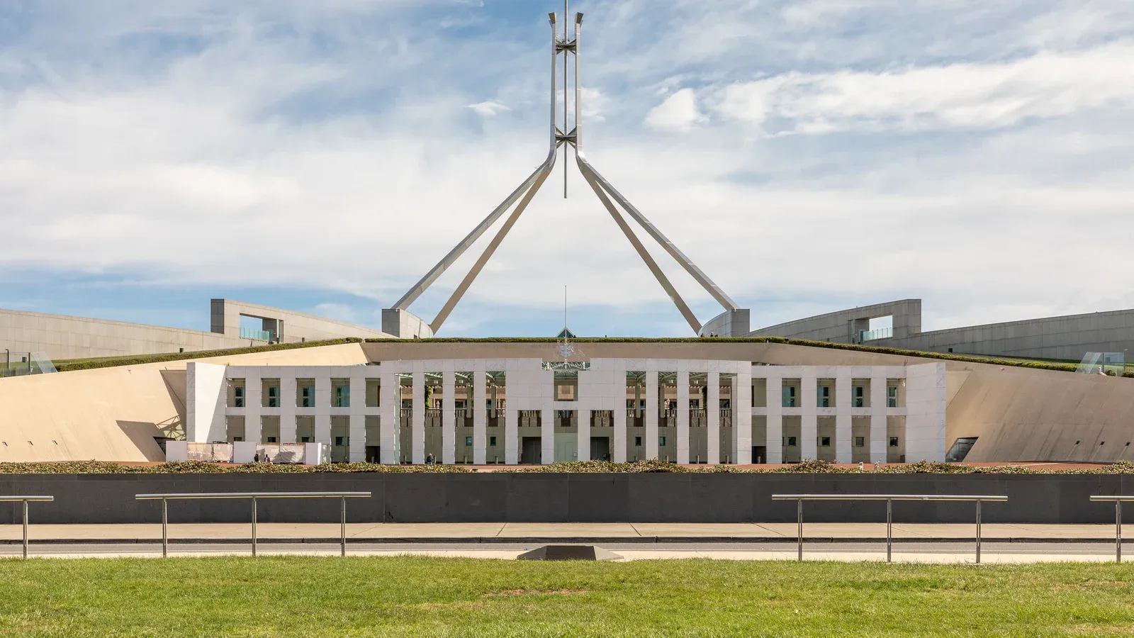 Parliament House in Canberra, seen across the water on 20 October 2019, with the Australian flag on the roof mast. Photo by Dietmar Rabich, CC BY-SA 4.0, via Wikimedia Commons.
